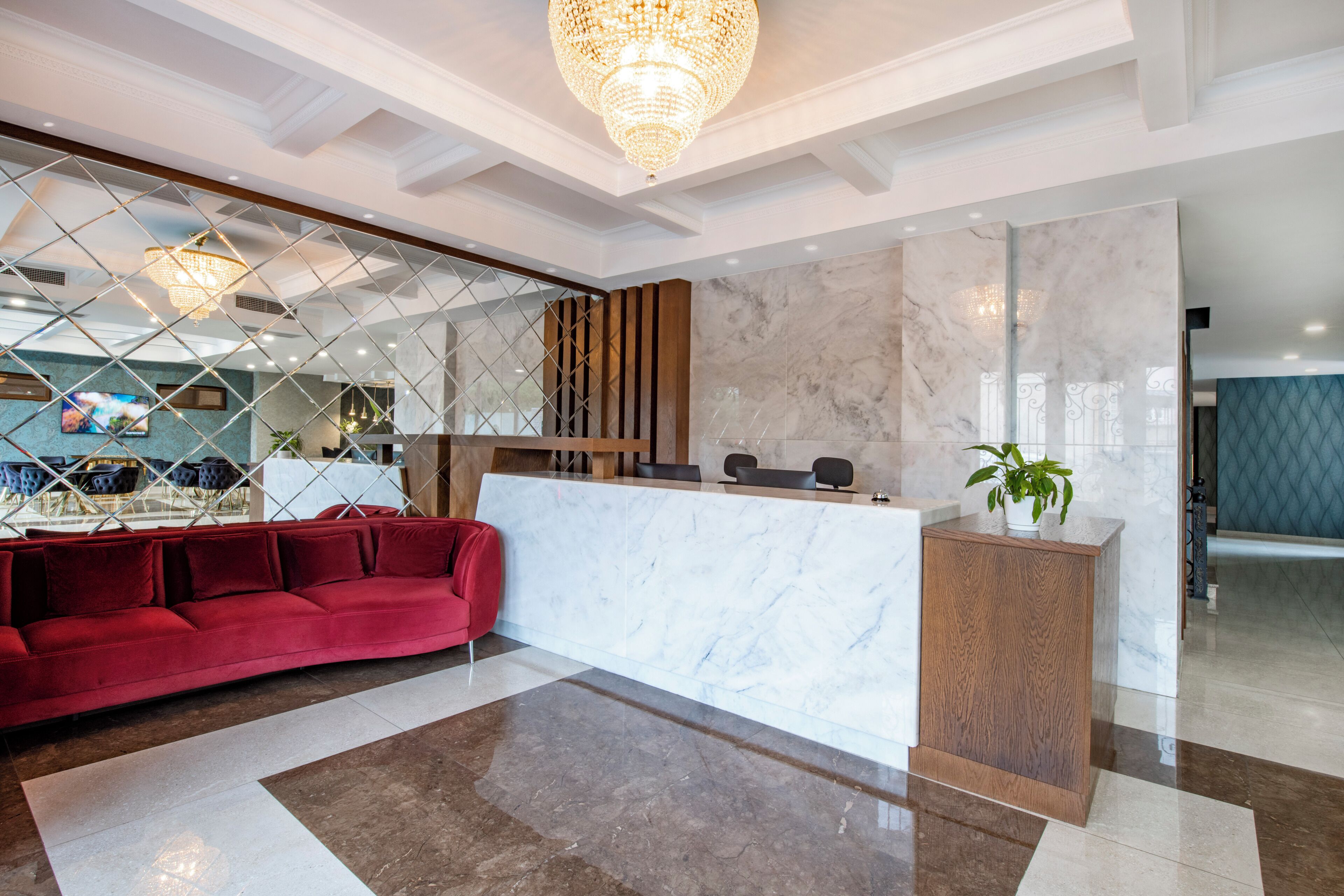 A reception area with a marble reception desk, a red sofa, a wooden panel wall, and a chandelier.