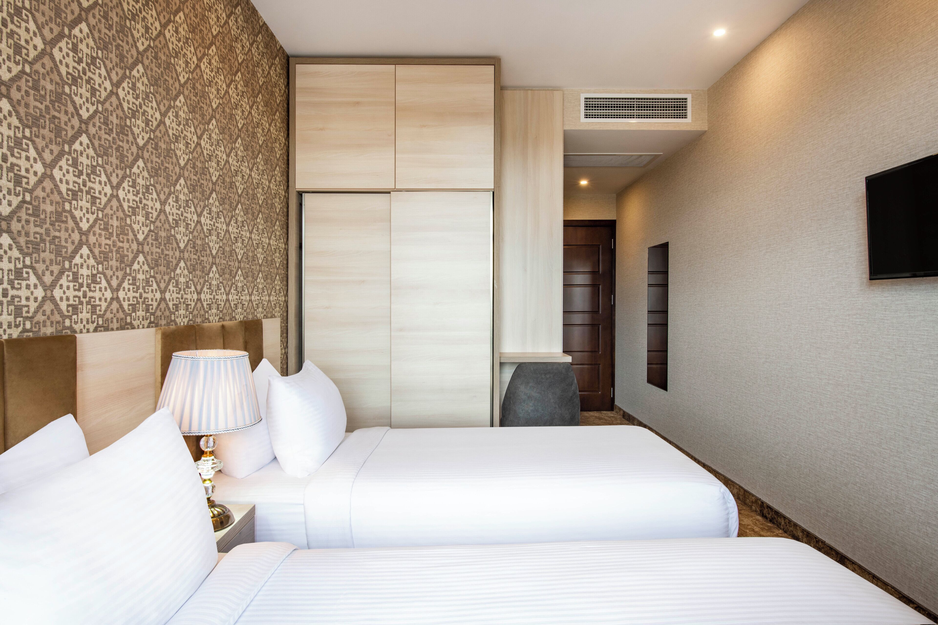 A hotel room with two beds, a patterned wall, a television, and a wardrobe.