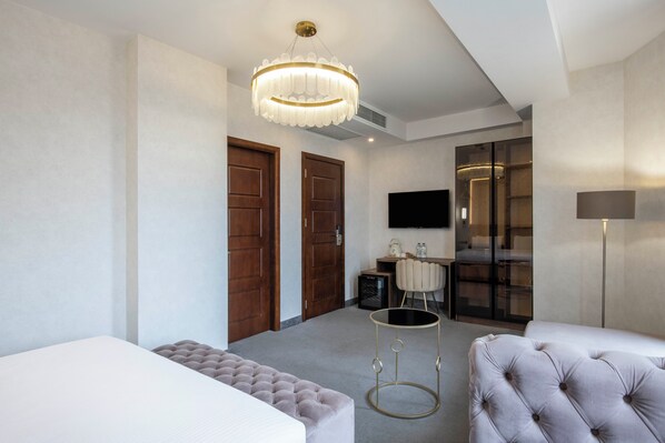 A hotel room with a bed, two seating areas, a television, a desk, and a wardrobe.