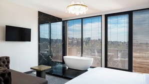 Une chambre moderne dotée d’un grand lit, d’une baignoire, d’un téléviseur à écran plat et offrant une vue sur la ville.