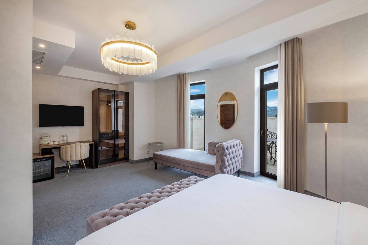 Une chambre d’hôtel avec un grand lit, un bureau, une chaise, une télévision, un lustre et une vue sur l’extérieur.