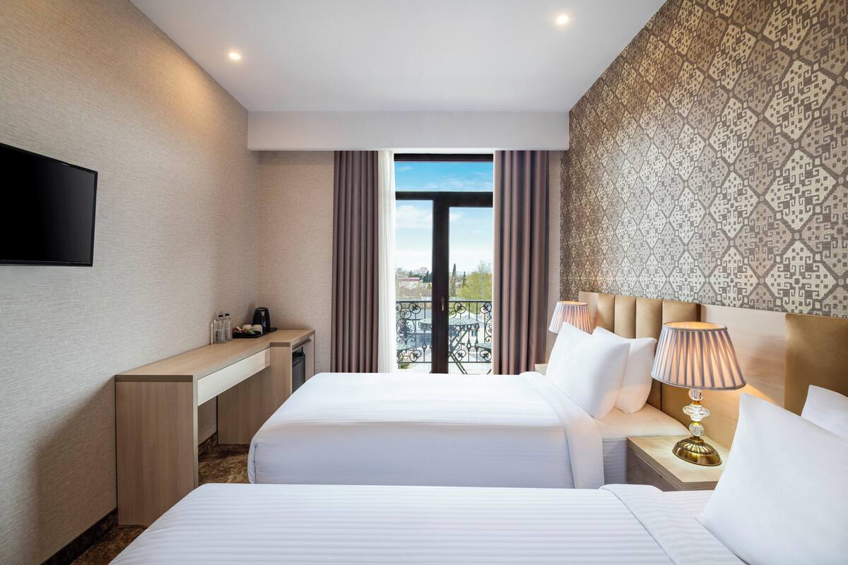 Une chambre d’hôtel avec deux lits, un bureau, une télévision et un balcon avec vue.