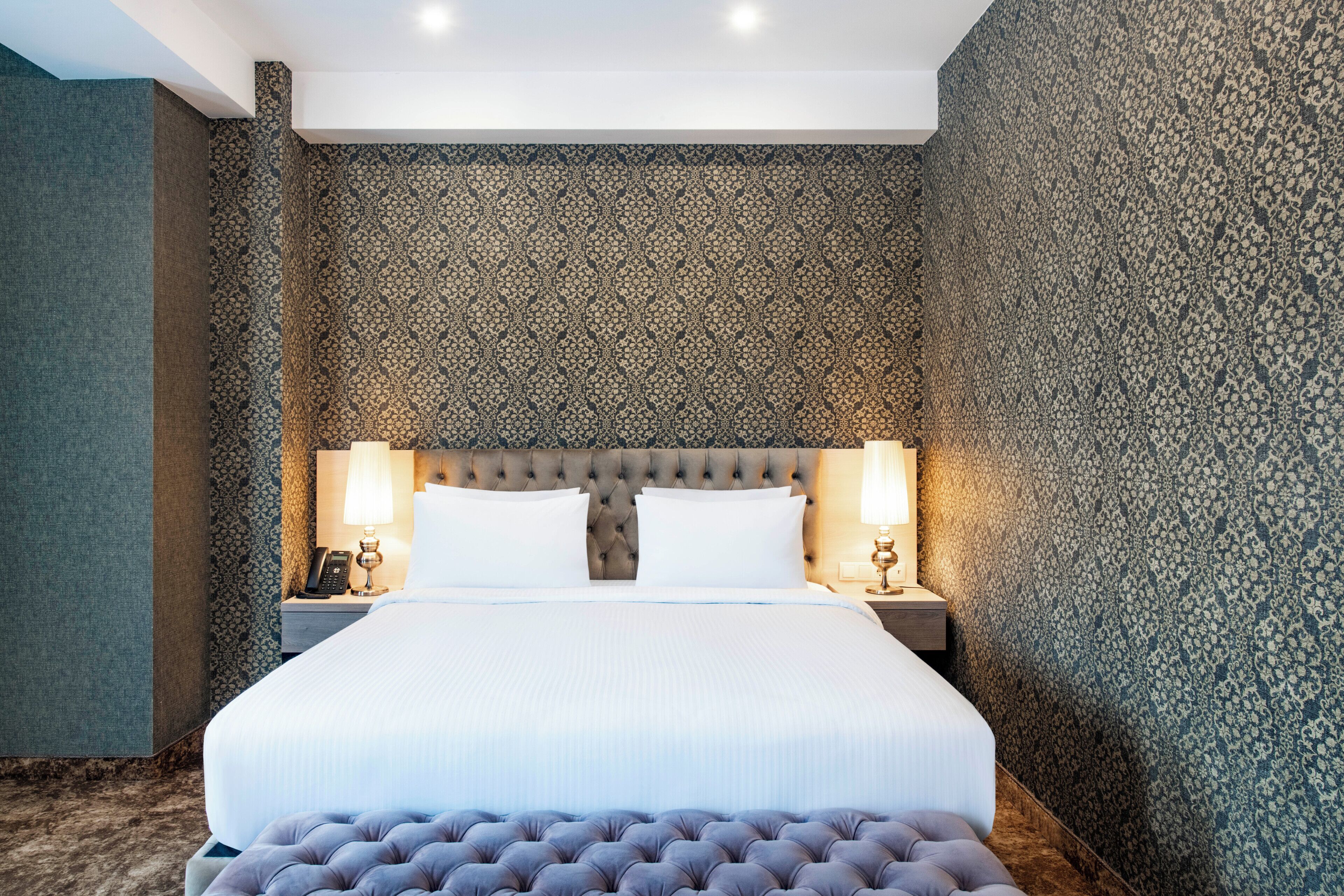 A neatly arranged hotel room with a large bed, two bedside tables, and a tufted bench.