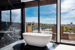 A modern bathroom with a freestanding bathtub, large windows, and a city view.