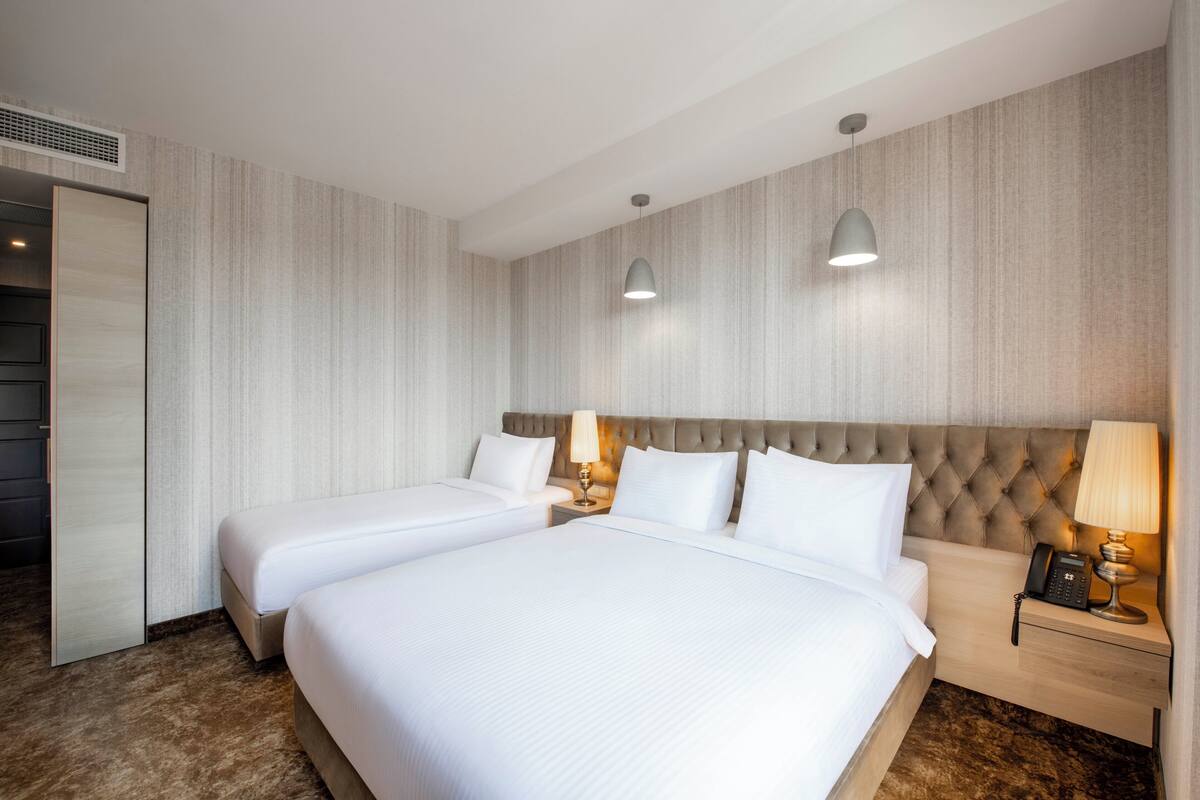 Une chambre d’hôtel avec deux lits, une grande tête de lit rembourrée, des lampes de chevet, un téléphone et une armoire.