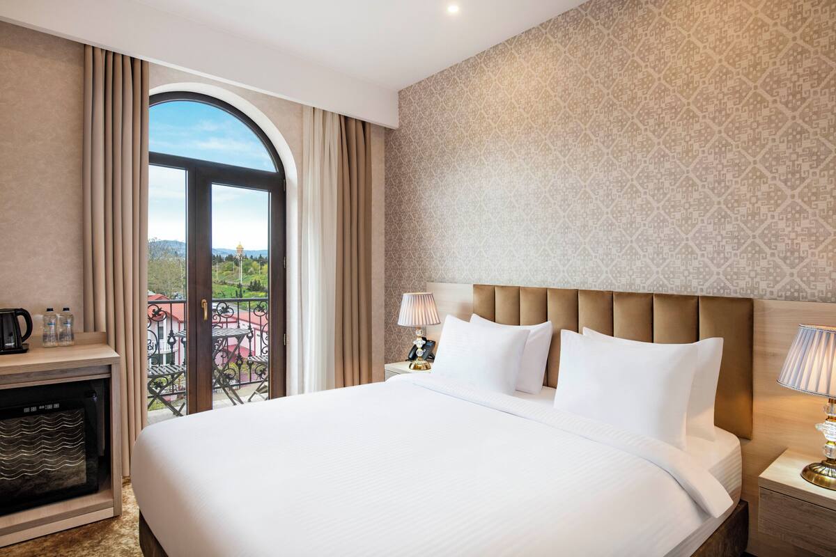 Une chambre d’hôtel avec un grand lit, une table de chevet, une lampe, une machine à café et une vue sur l’extérieur.