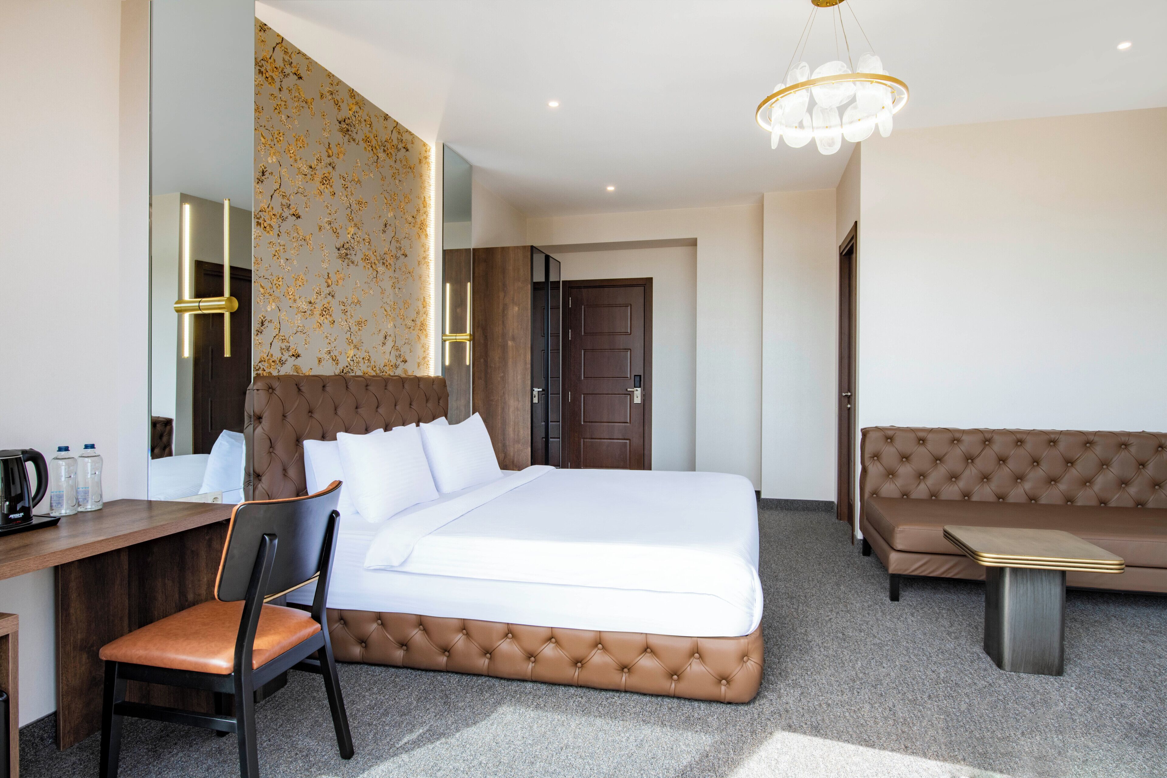 Een hotelkamer met een bed, een bureau, een stoel, een bank, een kroonluchter en een deur.