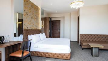 A hotel room with a bed, a desk, a chair, a sofa, a chandelier, and a door.