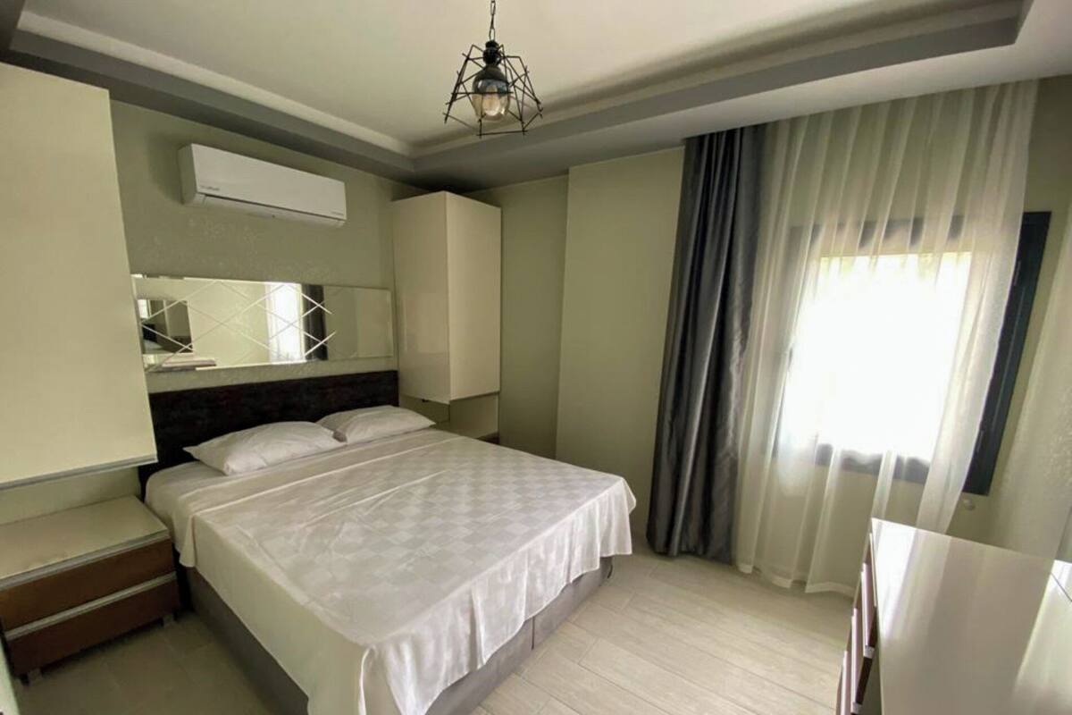 Une chambre d’hôtel avec un lit, un bureau, une chaise, un miroir et une fenêtre avec des rideaux.