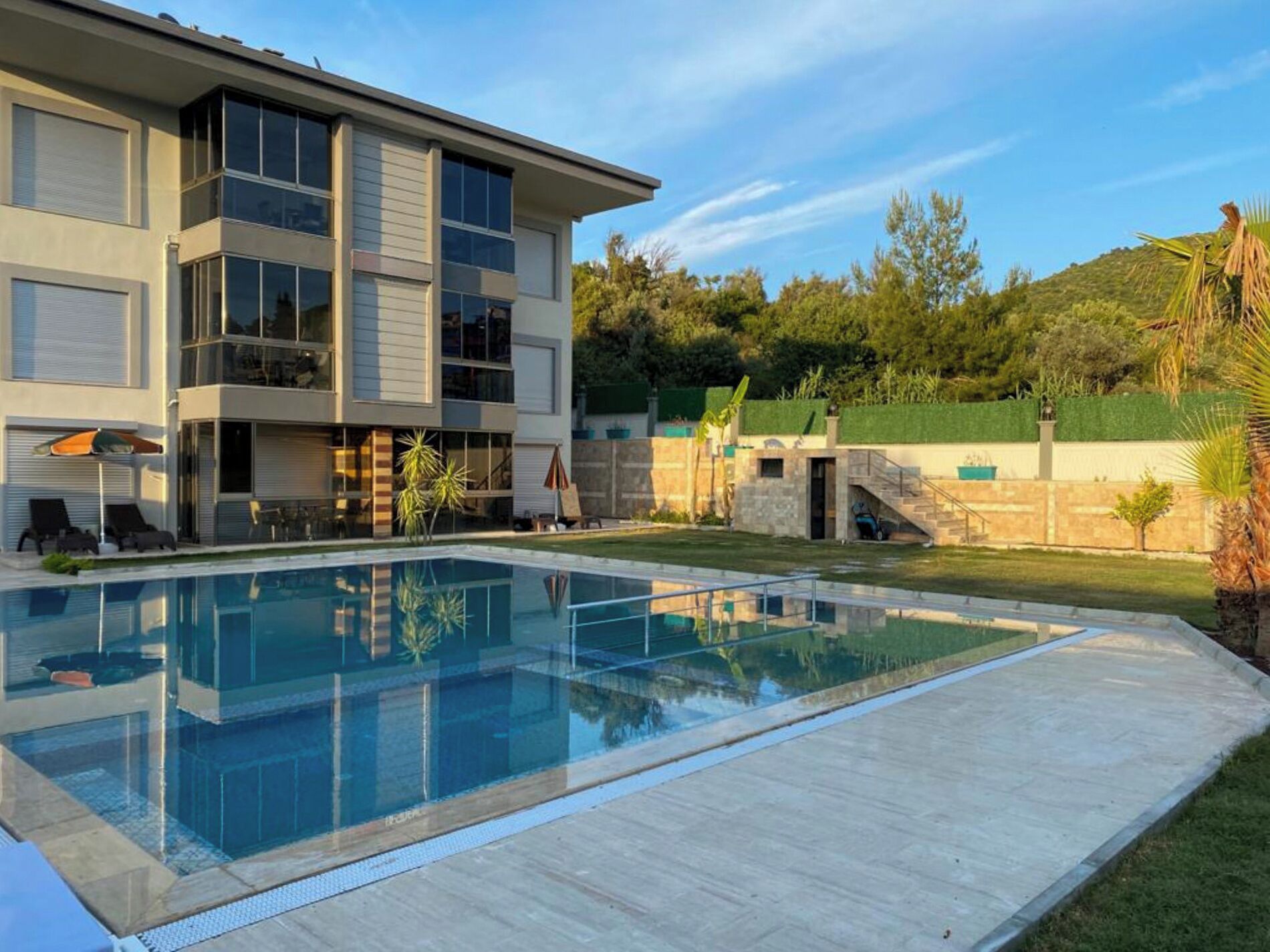 A modern two-story house with a swimming pool, outdoor seating, and a landscaped garden.