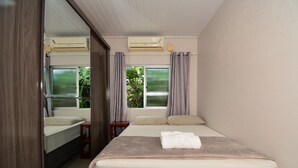 A bedroom with a bed, a bedside table, a mirror, an air conditioning unit, and a window with curtains.