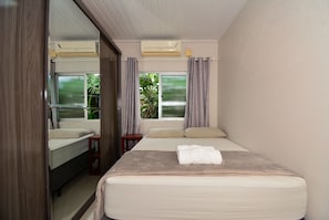 A bedroom with a bed, a bedside table, a mirror, an air conditioning unit, and a window with curtains.