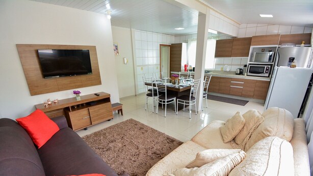 A modern living room with a flat-screen TV, a sofa, and a dining area with a table and chairs.