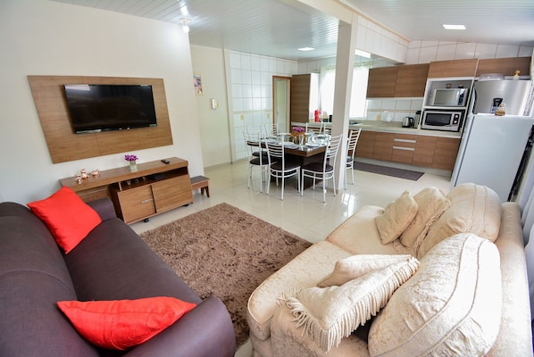 A modern living room with a flat-screen TV, a sofa, and a dining area with a table and chairs.