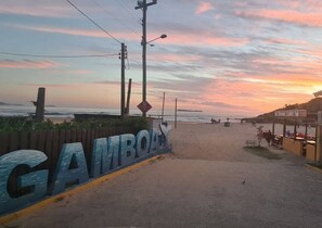 En väg som löper längs stranden, med en skylt som visar vägen till Gambia, och som leder till ett område med en strand och en restaurang.