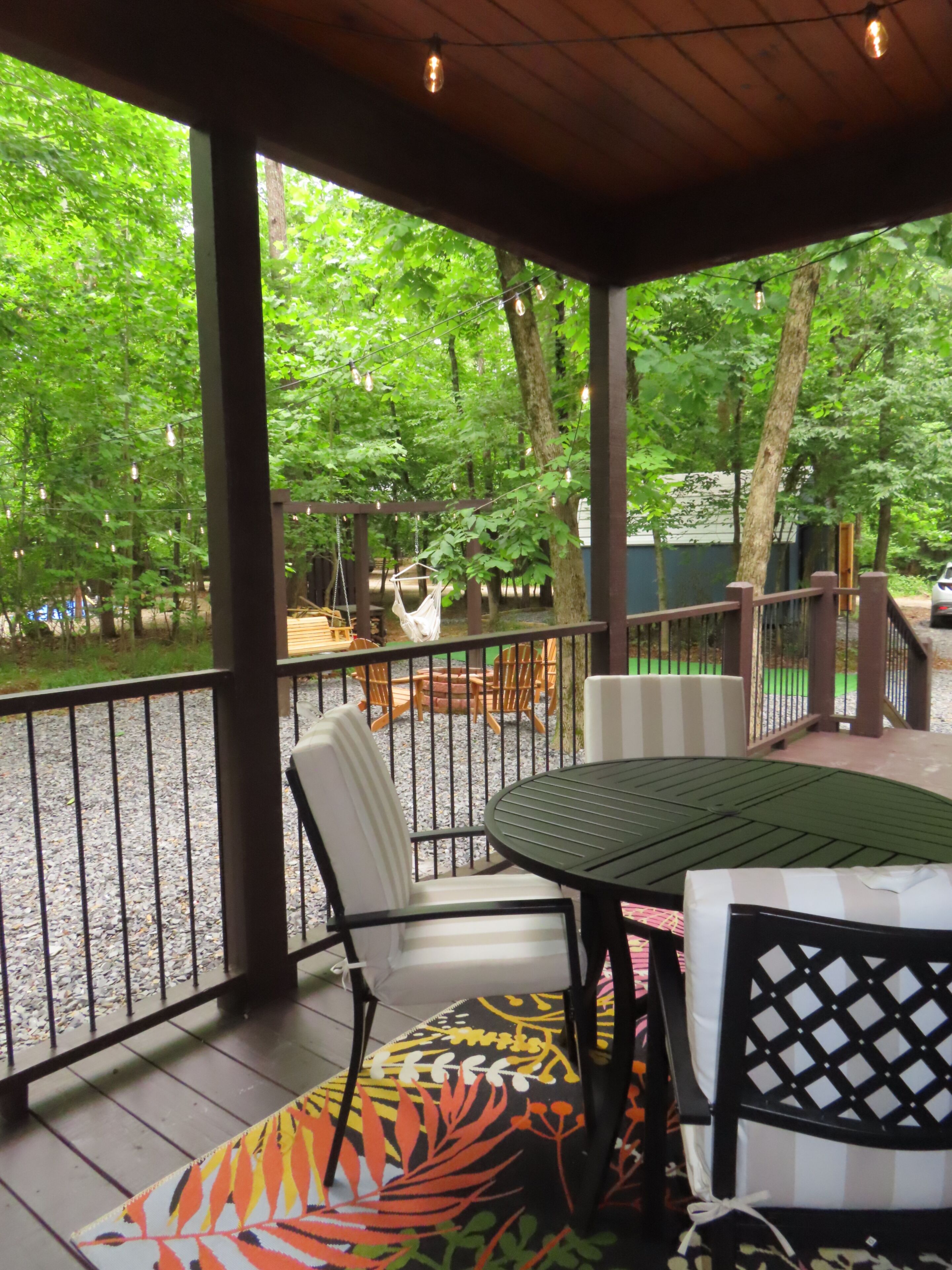 A covered outdoor area with a table and chairs, surrounded by a wooden fence and trees.