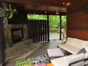 Eine Holzterrasse mit Kamin aus Stein, einer Couch und einem gemusterten Teppich.