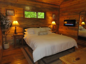 Ein Schlafzimmer in einer Holzhütte mit einem Bett, zwei Nachttischlampen, einem Nachttisch, einem Spiegel und einem Kamin.