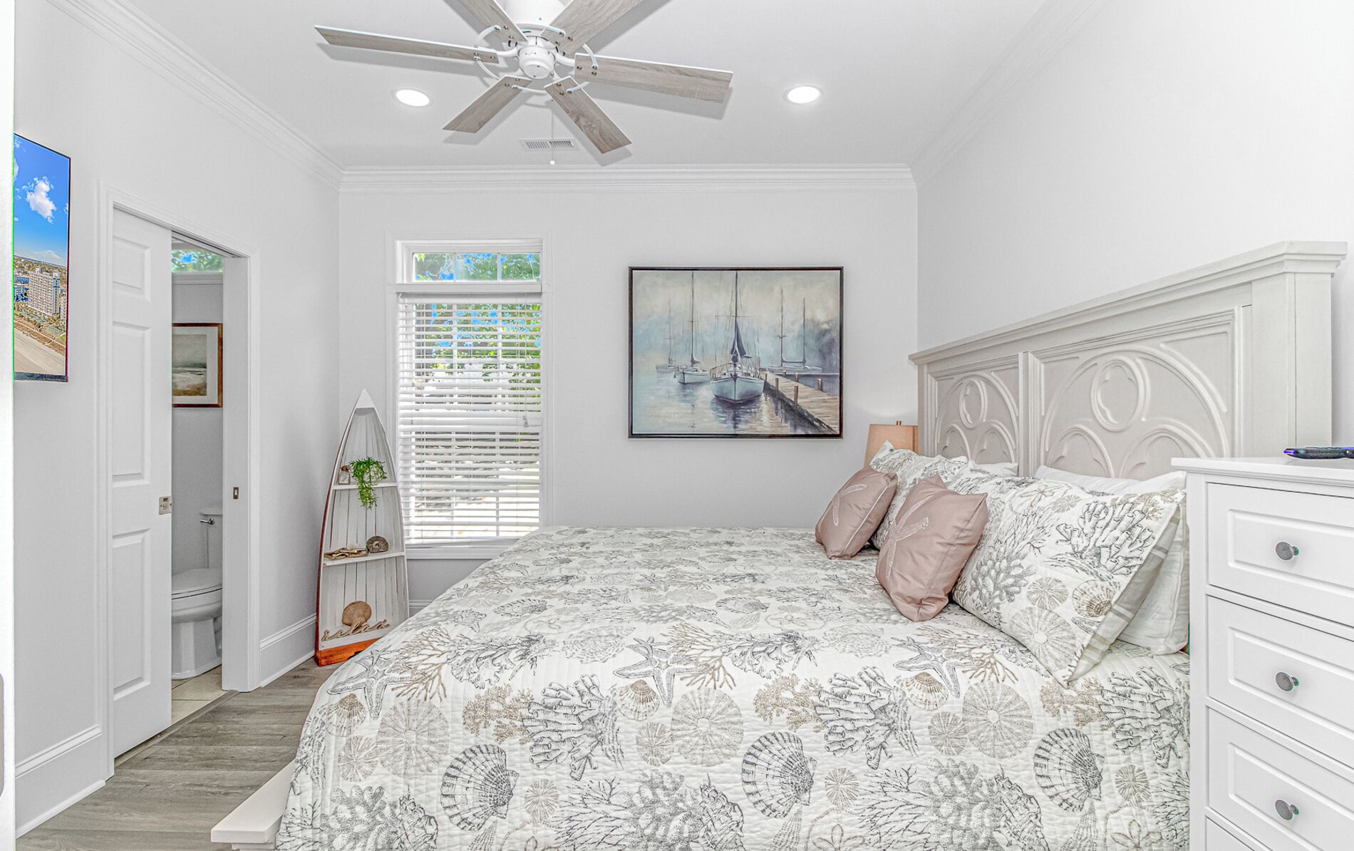 A bedroom with a bed, a ceiling fan, a window with blinds, a painting, and a nightstand.