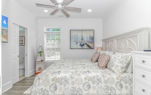 A bedroom with a bed, a ceiling fan, a window with blinds, a painting, and a nightstand. - Gorgeous 5-bdrm site 5713 Ocean Lakes golf cart interior elevator (Myrtle Beach)