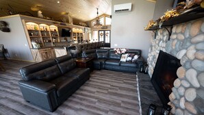 Een moderne woonkamer met een hoekbank, een stenen openhaard en een barruimte met flessen op planken.