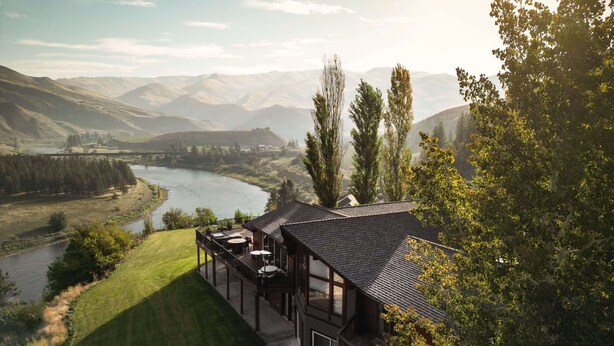 Een modern huis met een terras met uitzicht op een rivier en bergen.