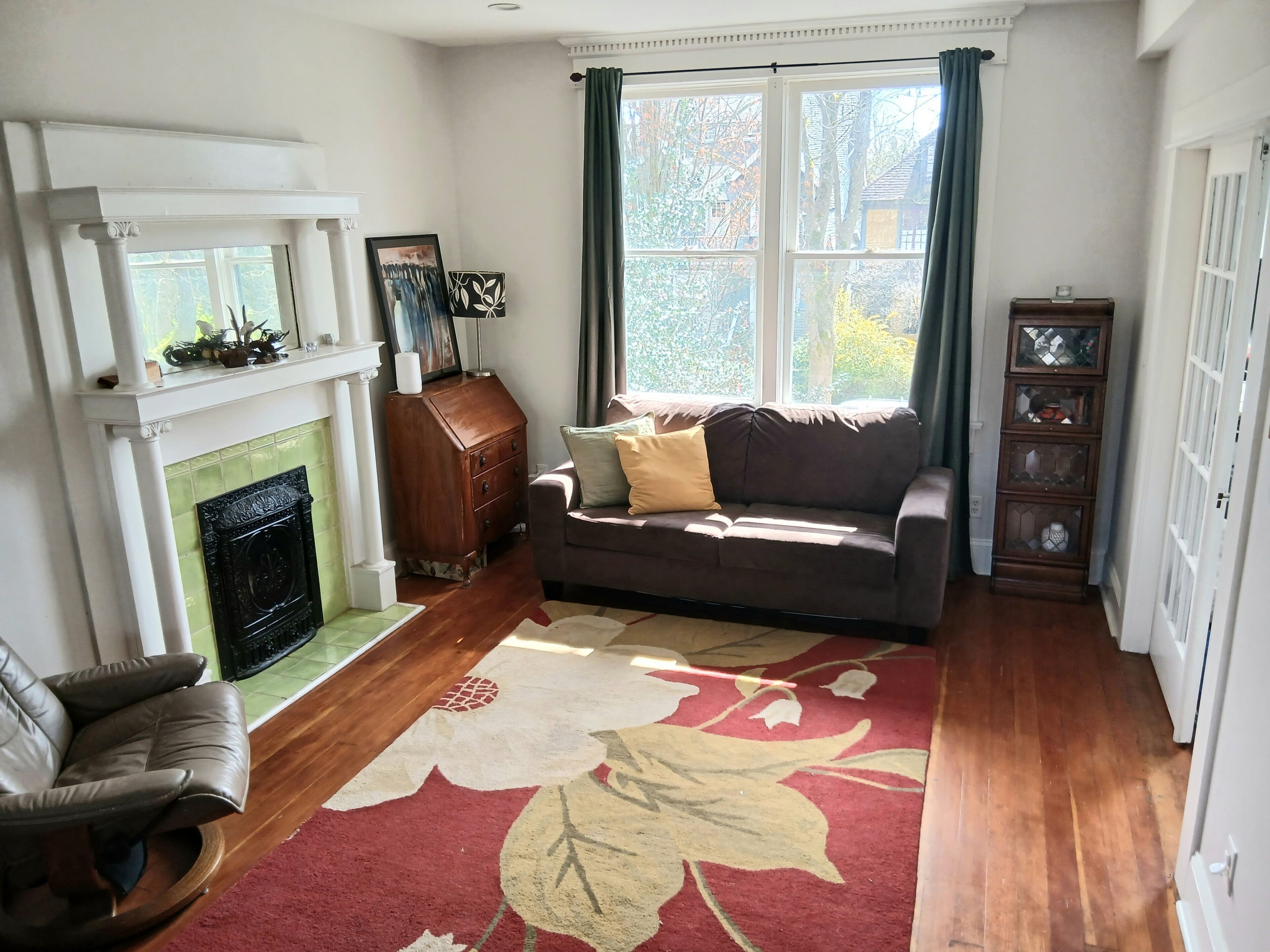 A living room with a fireplace, a sofa, a chair, a rug, and a window with curtains.