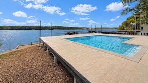 Une piscine rectangulaire avec une terrasse en bois, une jetée s’avançant dans un lac et un ciel dégagé.