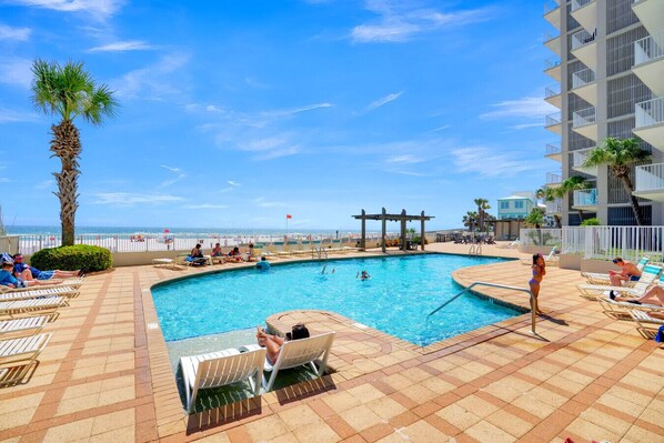 Ein Poolbereich mit Liegestühlen, einer Palme und Blick auf den Strand.