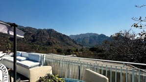 Un balcón con vistas a montañas, una silla blanca y una mesa con una planta.