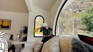 Una sala de estar con un sofá, una mesa de centro, un cuadro y una ventana con vistas al verdor.