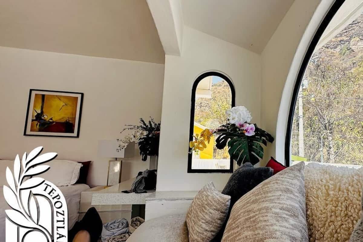 Ein Wohnzimmer mit einer Couch, einem Couchtisch, einem Gemälde und einem Fenster mit Blick auf Grünflächen.
