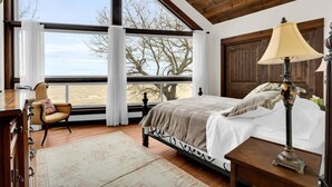 Une chambre avec une grande fenêtre, un lit, une chaise, une lampe et un plafond en bois.