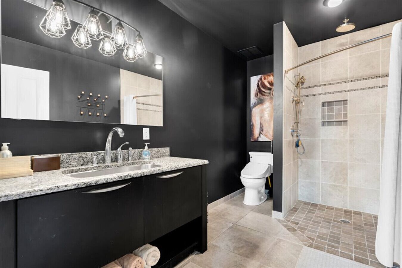 Une salle de bain moderne avec un comptoir en granit, un grand miroir et une douche dotée d’une porte en verre.