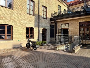 Ein Backsteinhaus mit einem Motorrad vor der Fassade, einem Balkon mit schmiedeeisernem Geländer und einem kleinen Garten.