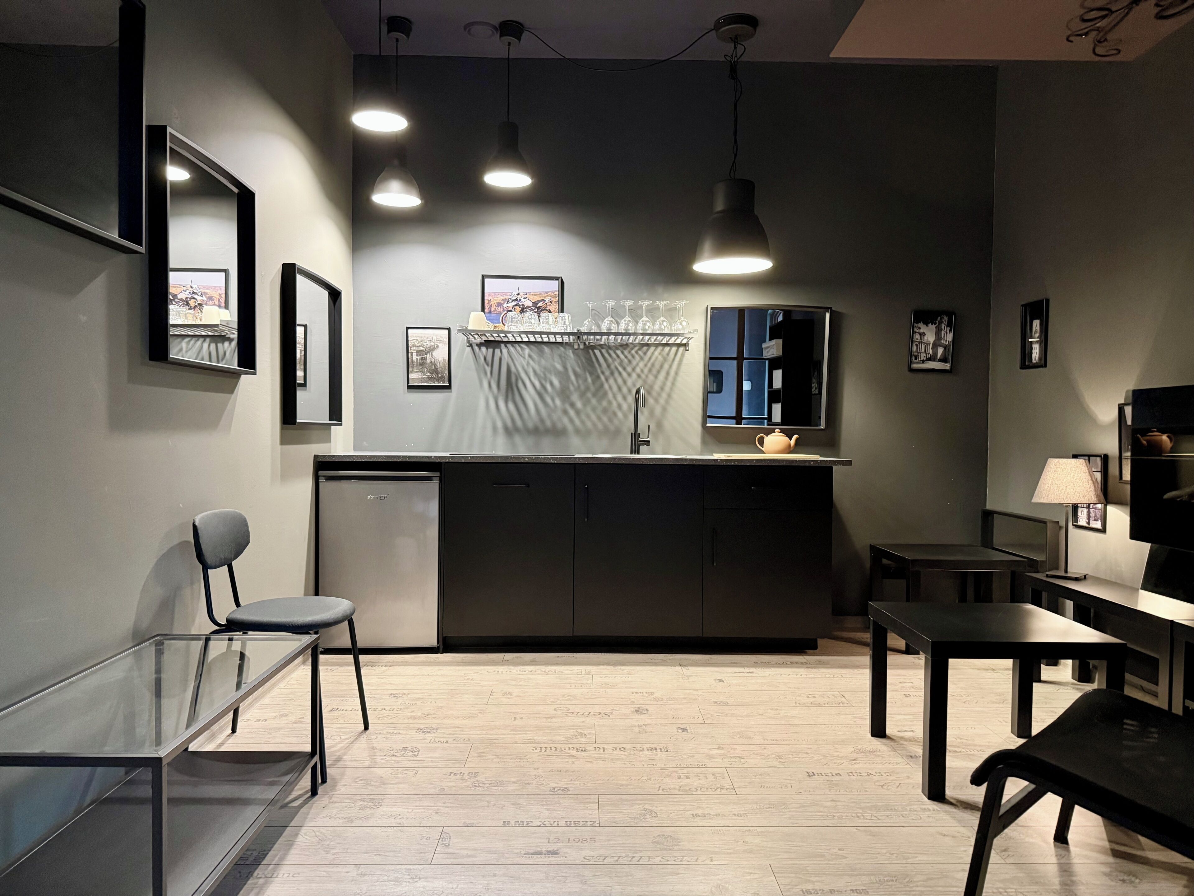 Une cuisine moderne équipée d’un lave-vaisselle encastré, d’un évier et d’un plan de travail sur lequel se trouve une théière. On y trouve également des luminaires suspendus, des tableaux encadrés au mur et un coin repas avec une table et des chaises.