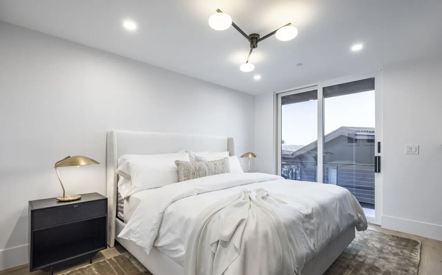 Une chambre moderne avec un grand lit, des lampes de chevet, une table de nuit et une vue sur l’extérieur grâce à une porte-fenêtre coulissante.