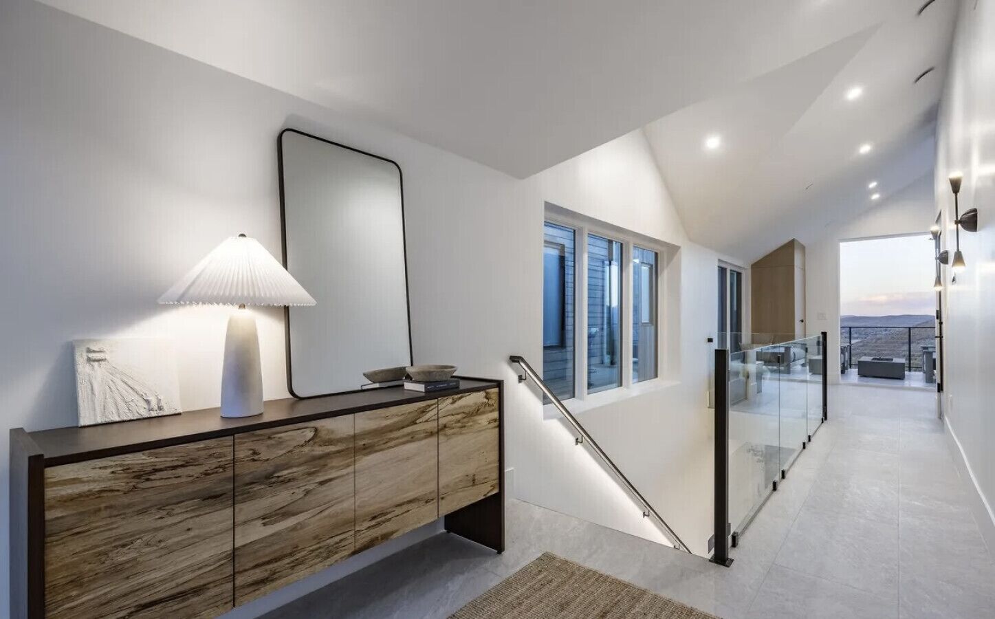 A modern interior with a marble console, a wall-mounted mirror, and a staircase leading to a balcony with a view.