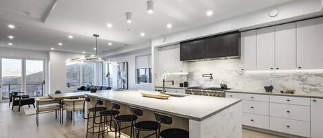 A modern kitchen with a large island, bar stools, and a dining area with a view.