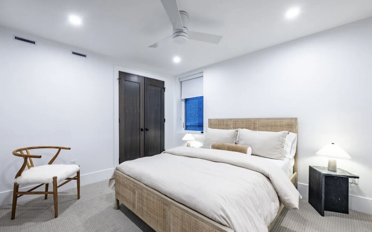 A bedroom with a bed, a chair, a nightstand, a window, and a ceiling fan.