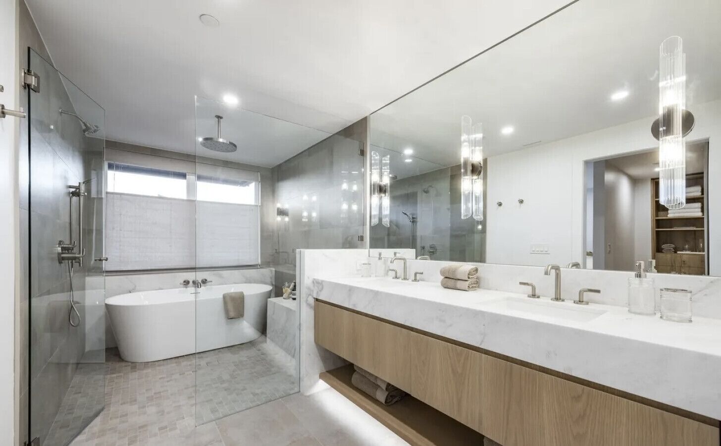 A modern bathroom with a glass-enclosed shower, a freestanding bathtub, and a large vanity with a mirror.