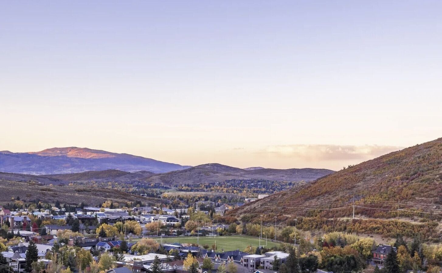 A town with houses, a green field, and mountains in the background.