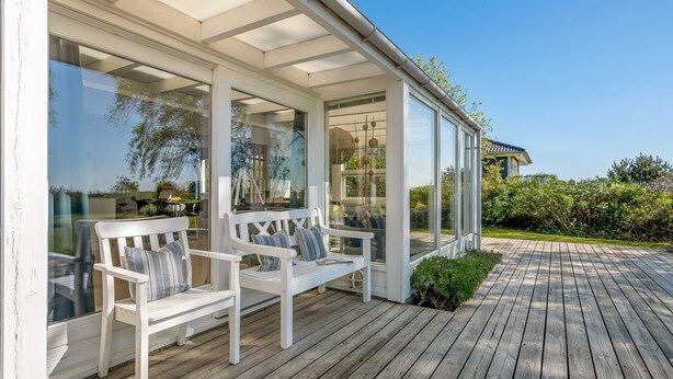 Een overdekt terras met witte banken en een houten vlonder.