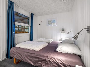 Un dormitorio con cama, ventana con cortinas, lámpara de pared y una planta pequeña.