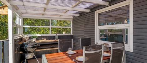 Un patio exterior con mesa y sillas de madera, una parrilla y una ventana con vistas a la vegetación.