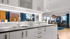 Een moderne keuken met witte kasten, een roestvrijstalen spoelbak en een groot raam met blauwe gordijnen.
