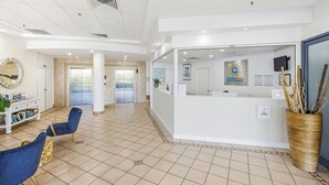 A reception area with a white counter, a reception desk, a blue chair, a large mirror, and a decorative vase with sticks. - Centrepoint Unit 58, 30 Minchinton Street, Calound (Caloundra)