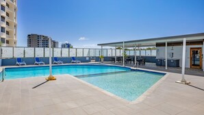 A swimming pool with lounge chairs, a covered seating area, and a view of surrounding buildings. - Centrepoint Unit 58, 30 Minchinton Street, Calound (Caloundra)