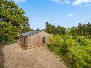 Eine Holzhütte mit einer Schotterauffahrt, umgeben von dichten Bäumen und Grün.