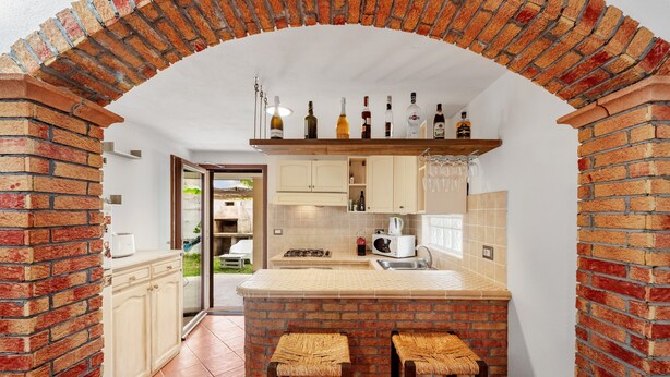 Una cocina con un arco de ladrillo, una zona de bar con taburetes y una variedad de botellas en la estantería.